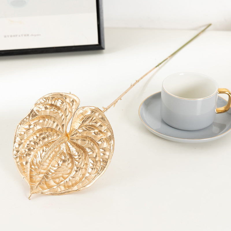 Gold leaf-shaped coaster on a white surface with a cup and saucer in the background.