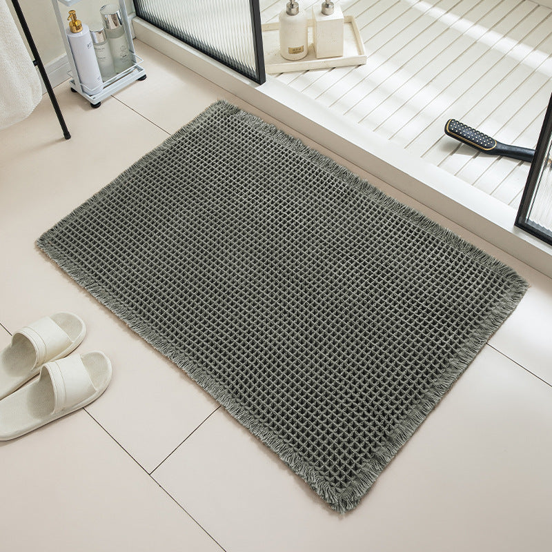 Gray doormat on a tiled floor with white slippers and a remote control nearby.