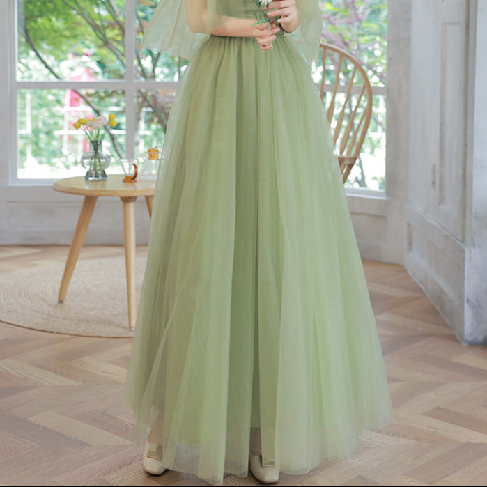 Woman in a light green dress standing in a room with large windows and a wooden floor.
