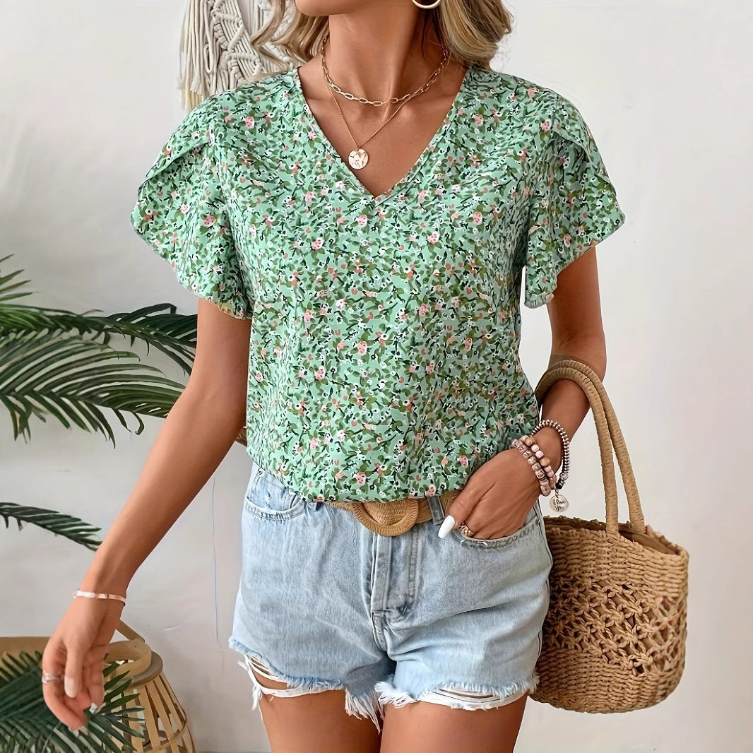 Woman wearing a green floral top and denim shorts, holding a woven bag.