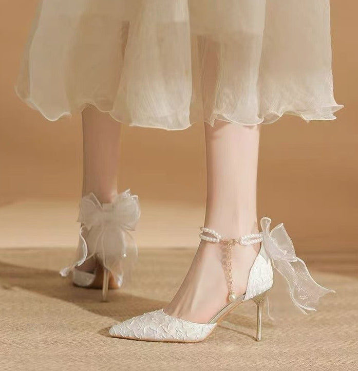 White lace high-heeled shoes with ribbons worn with a light-colored dress on a neutral background
