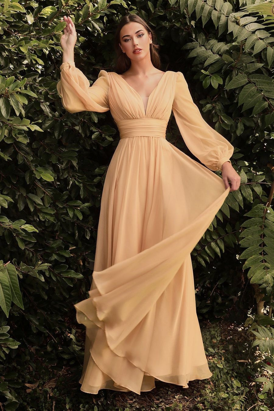 Woman in a long, flowing beige dress standing against a green leafy background