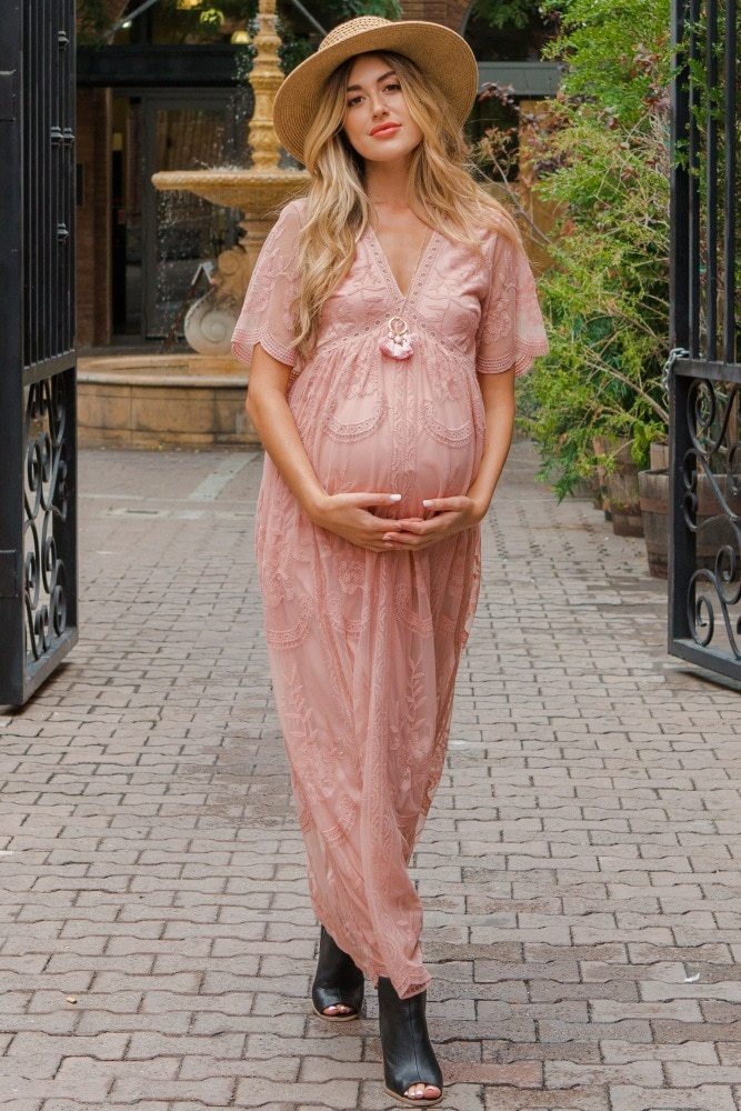 Pregnant woman in a pink dress standing outdoors on a paved path.