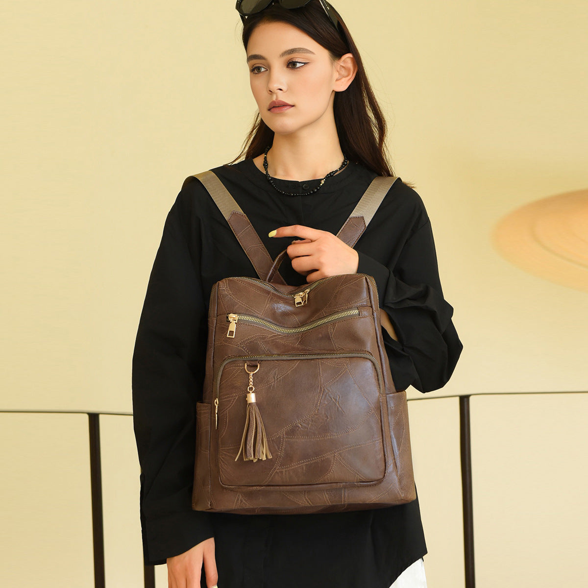 Woman holding a brown leather backpack against a beige background