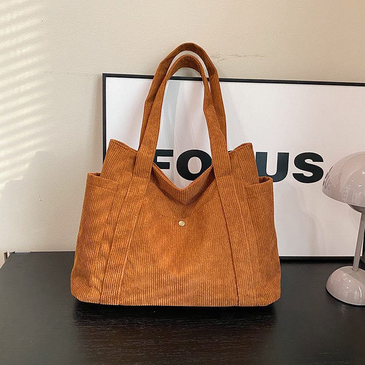 Brown corduroy tote bag on a black surface with a white wall and lamp in the background.