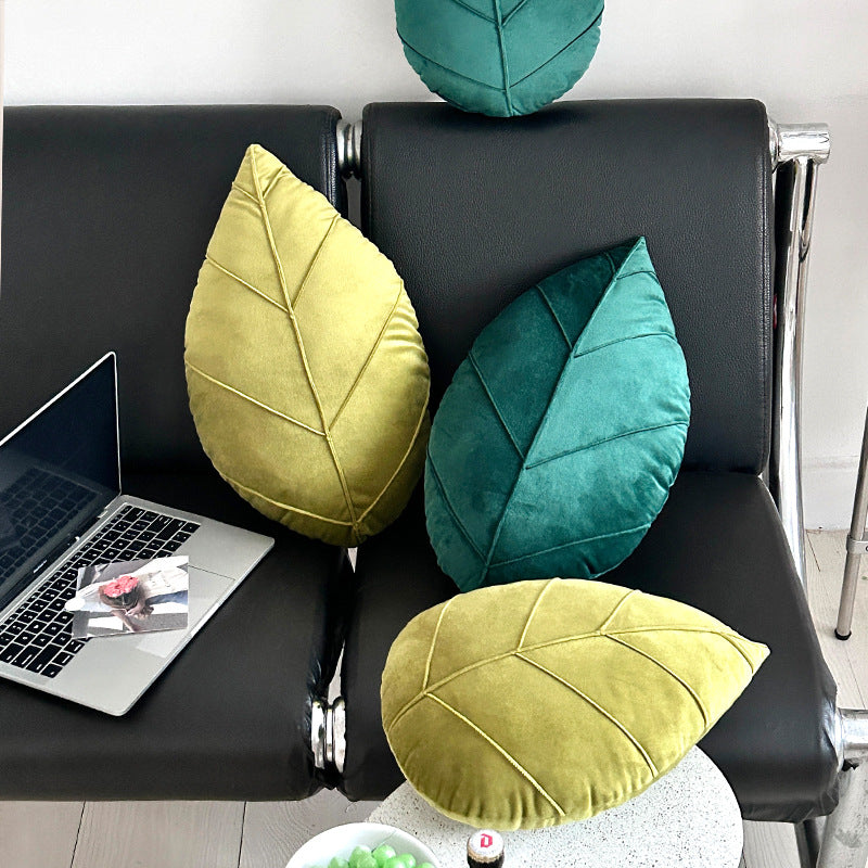 Leaf-shaped pillows in green and yellow on a chair next to a laptop.