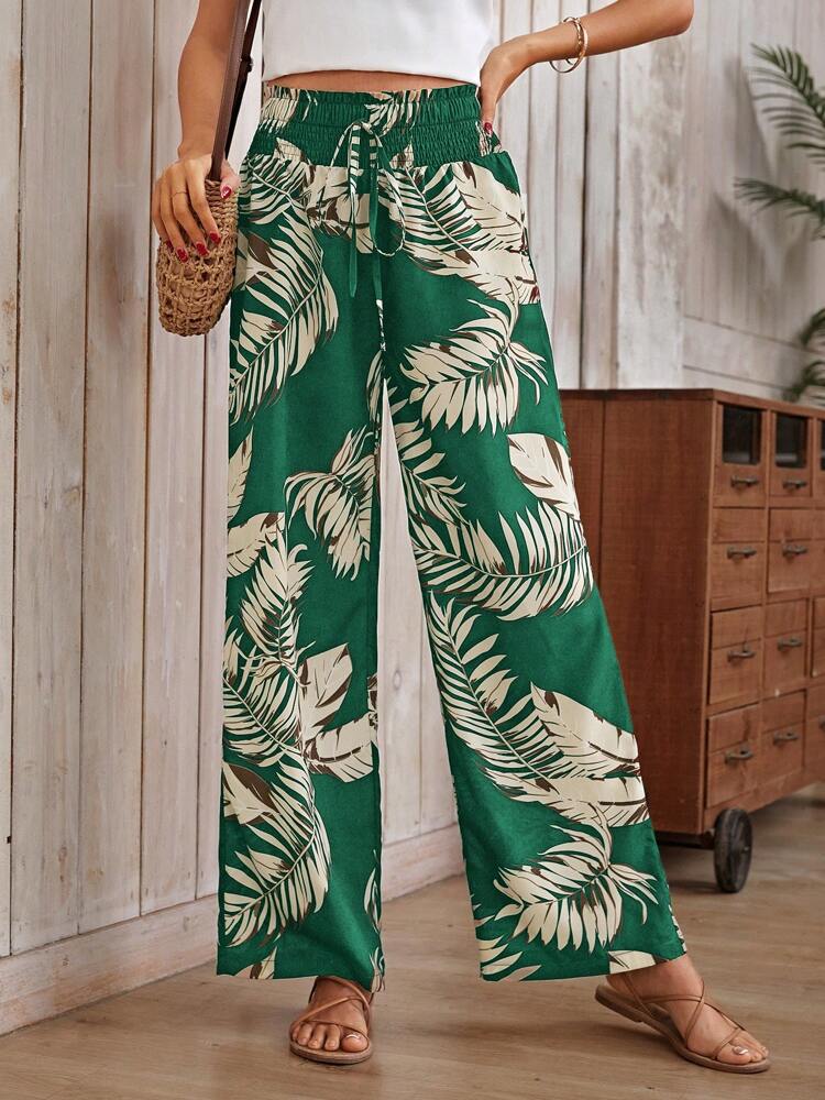 Person wearing green leaf-patterned pants in a room with wooden floor and furniture.