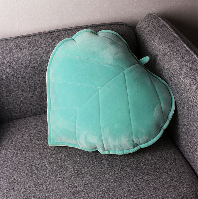 Turquoise leaf-shaped pillow on a gray couch