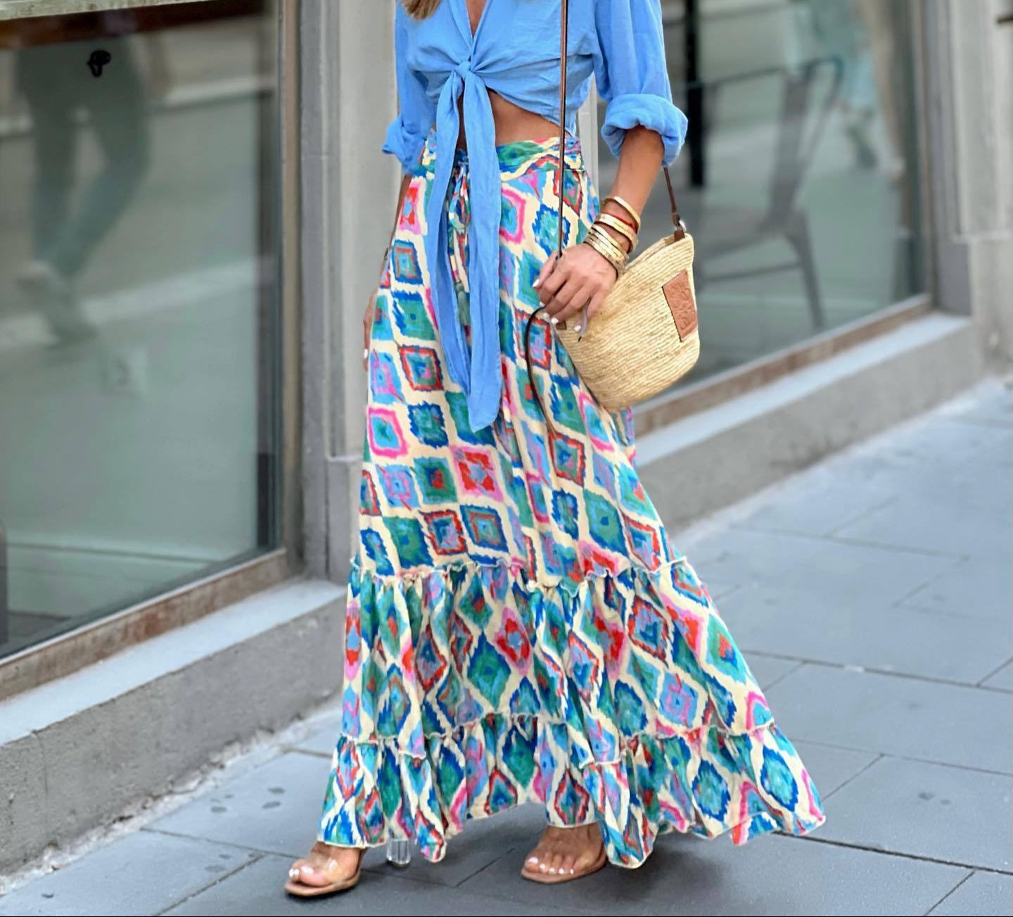 Woman wearing a blue top and colorful patterned skirt on a city street.