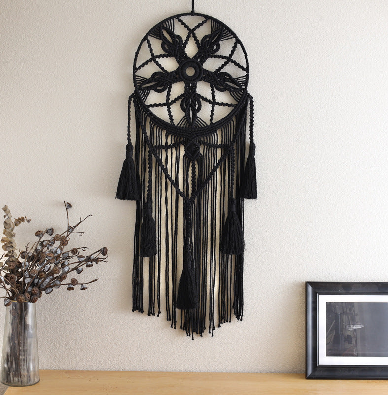 Black dreamcatcher hanging on a white wall with a vase and framed picture below.