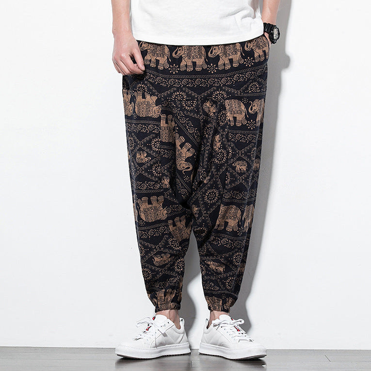 Person wearing black pants with elephant pattern and white sneakers on a white background