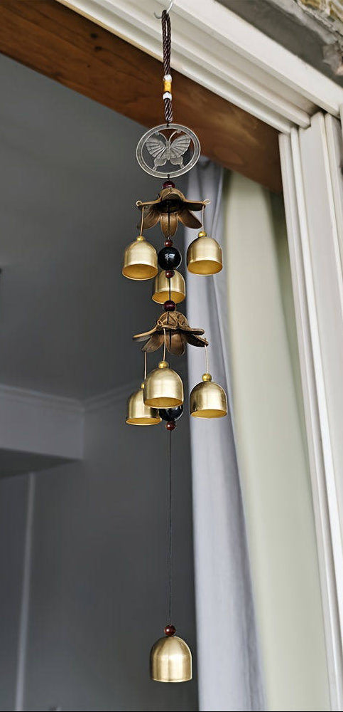 Decorative hanging bell chime with butterfly design in a room with a window and ceiling light fixture.