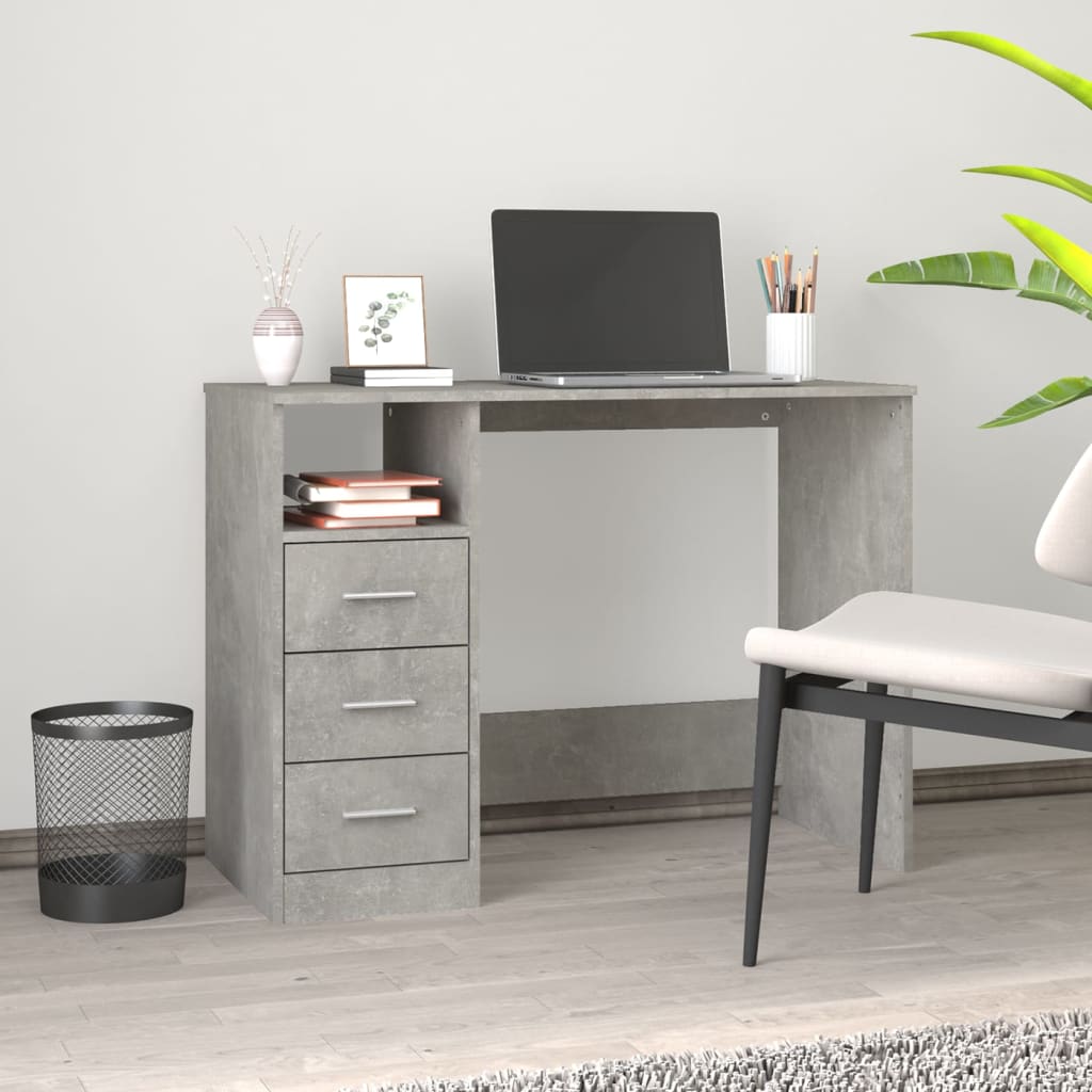 Gray concrete-style desk with a laptop, books, and a plant in a room with a chair and trash can.