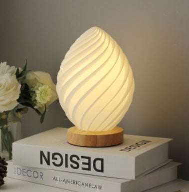 Egg-shaped lamp on books with flowers and decorative items in the background