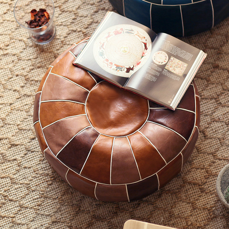 Brown leather ottoman with an open book on a textured surface
