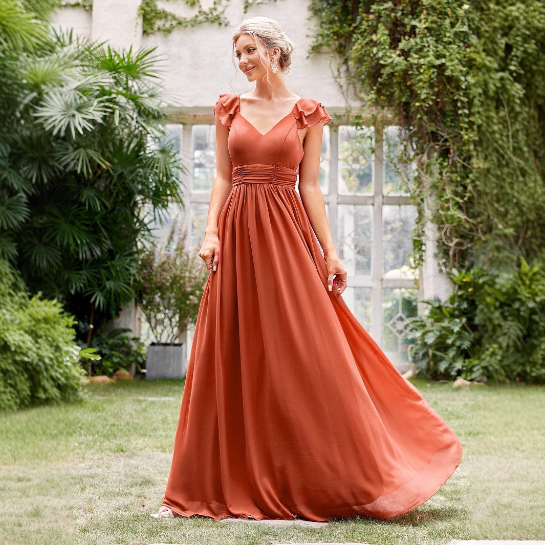 Woman in a long orange dress standing outdoors with greenery around