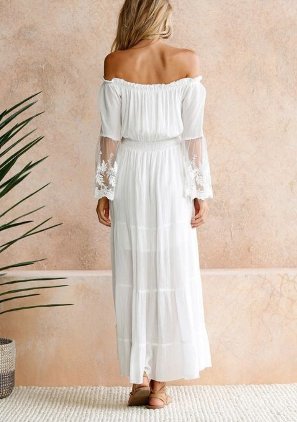 Woman wearing a white off-shoulder dress against a beige wall.