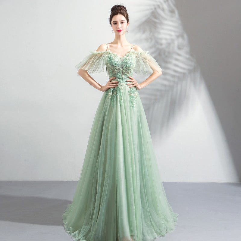 Woman wearing a light green evening gown with sheer sleeves against a neutral background