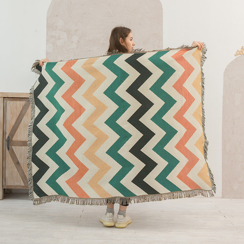 Person holding a colorful zigzag patterned blanket in a room with a wooden cabinet.