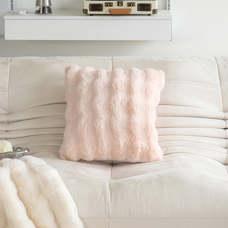 Pink fluffy pillow on a white couch with a white wall in the background