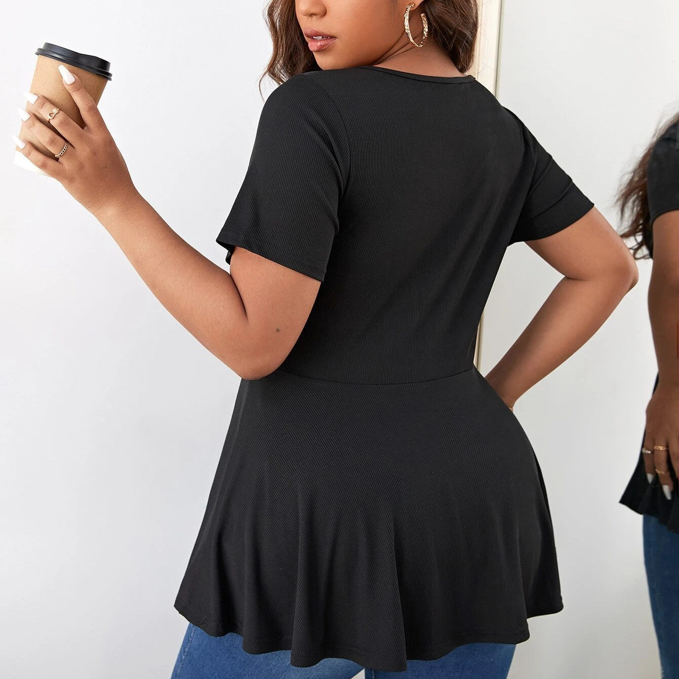 Woman wearing a black peplum top holding a coffee cup against a white background