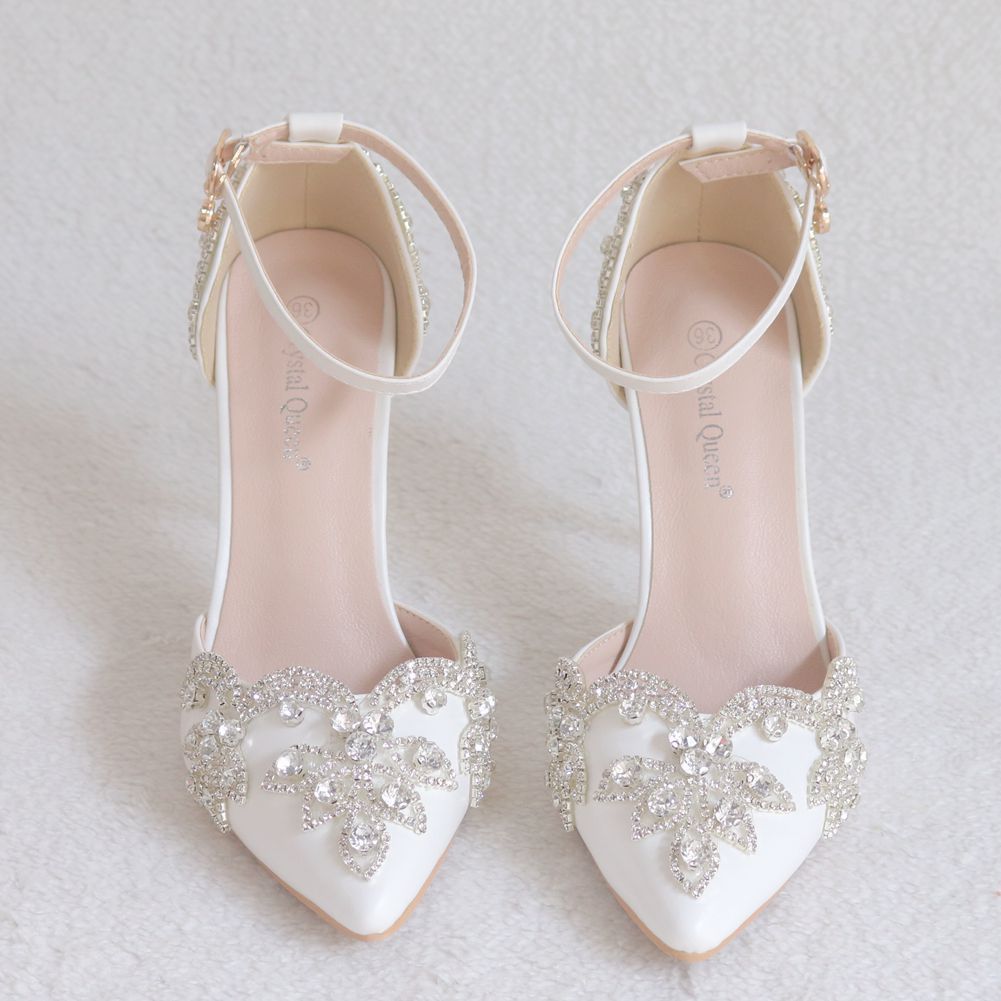 Pair of white wedding shoes with embellishments on a light gray background