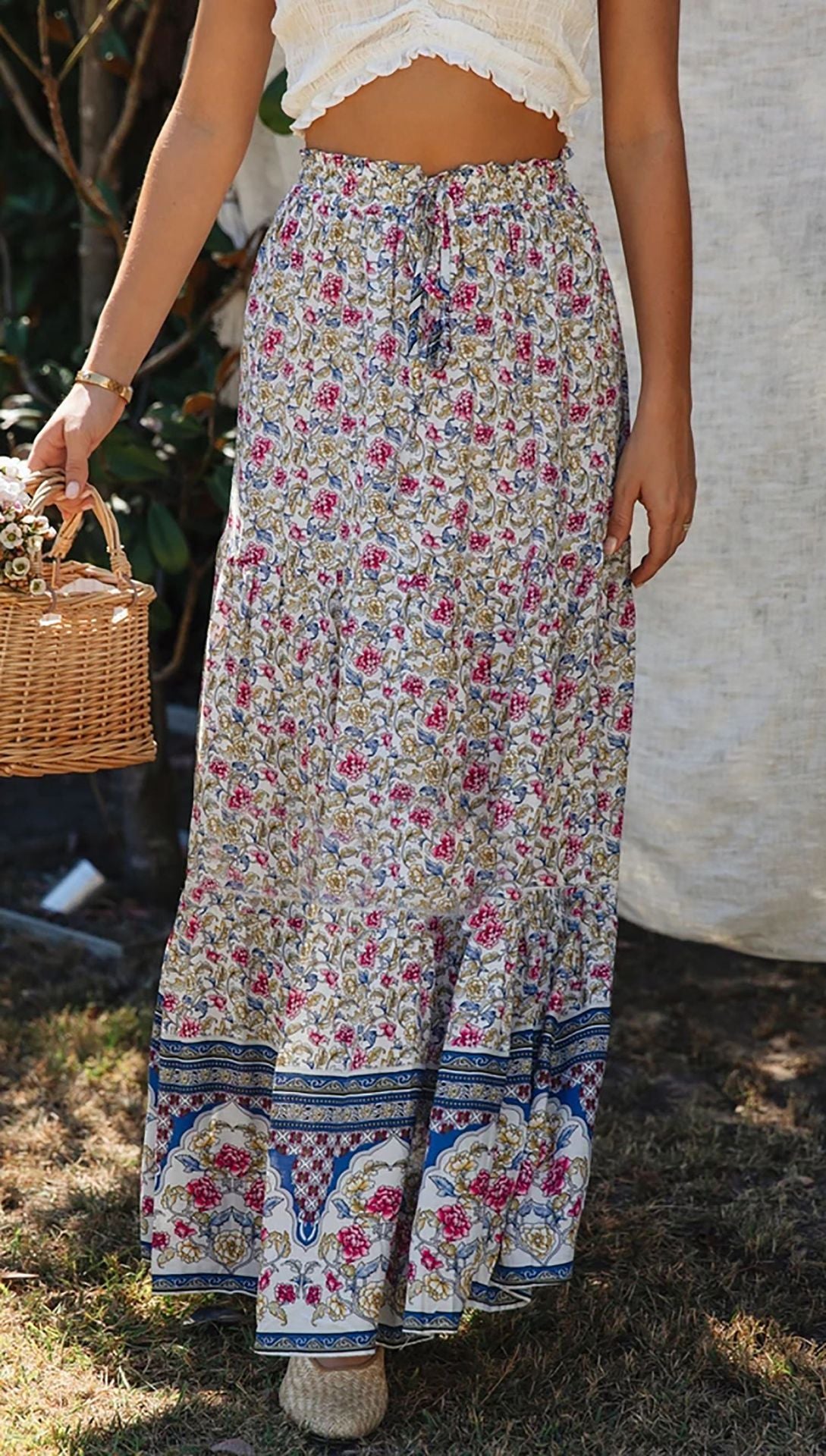 Person wearing a long floral skirt holding a woven basket outdoors.
