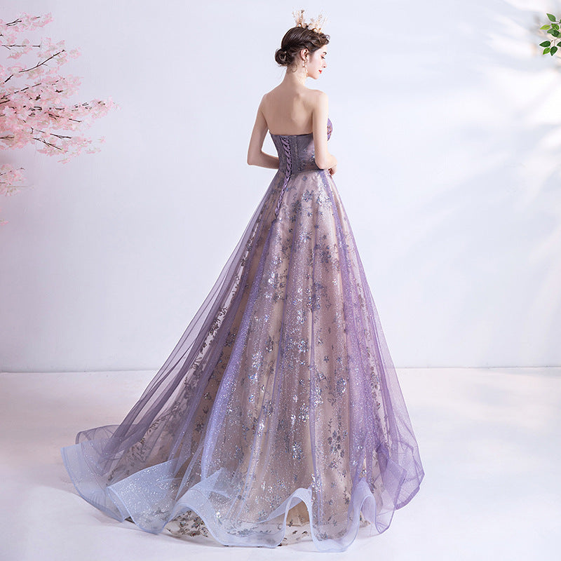 Woman in a strapless, long, light purple evening gown with floral details against a white background.