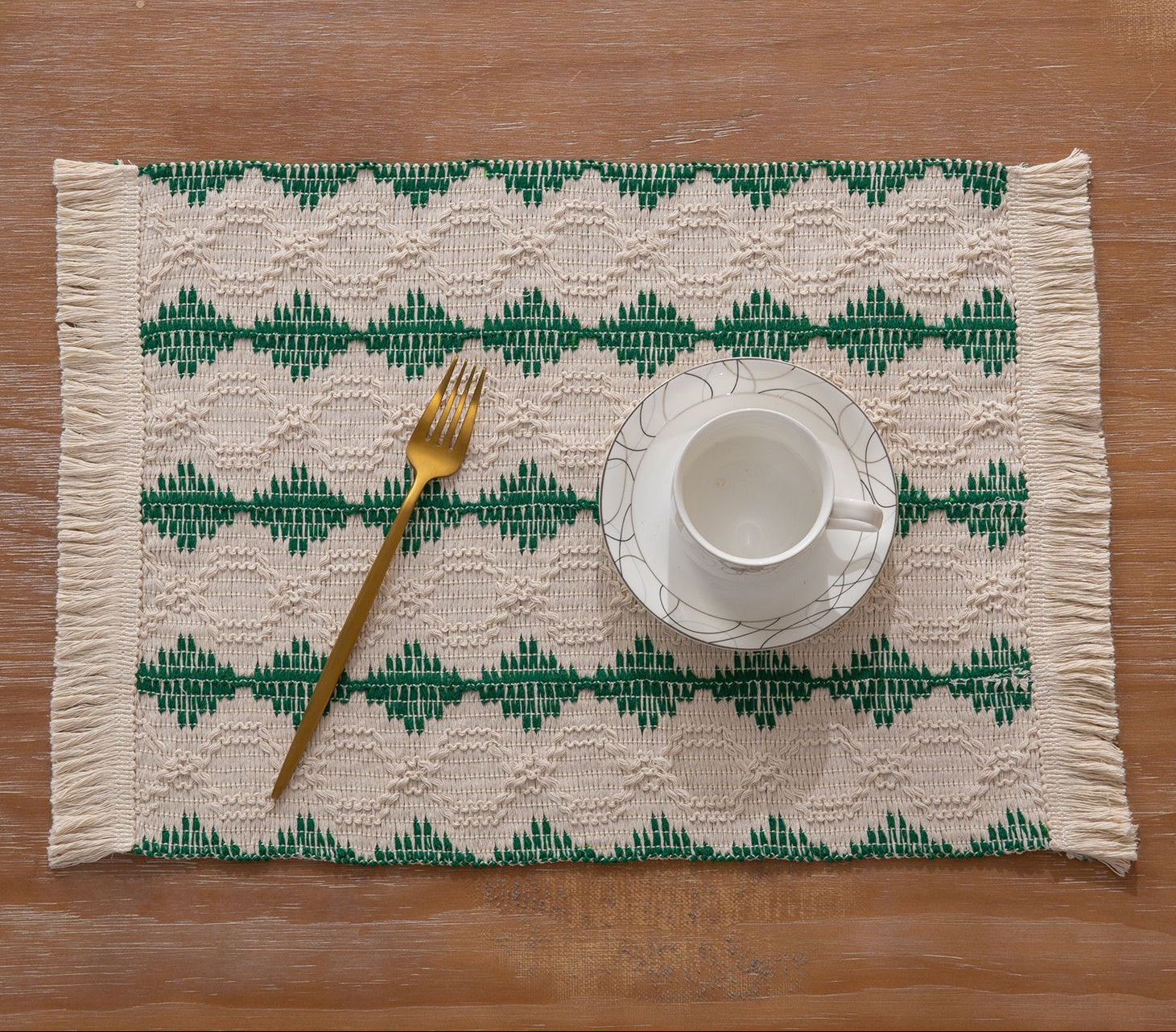Placemat with green geometric pattern on a wooden table with a cup and fork.