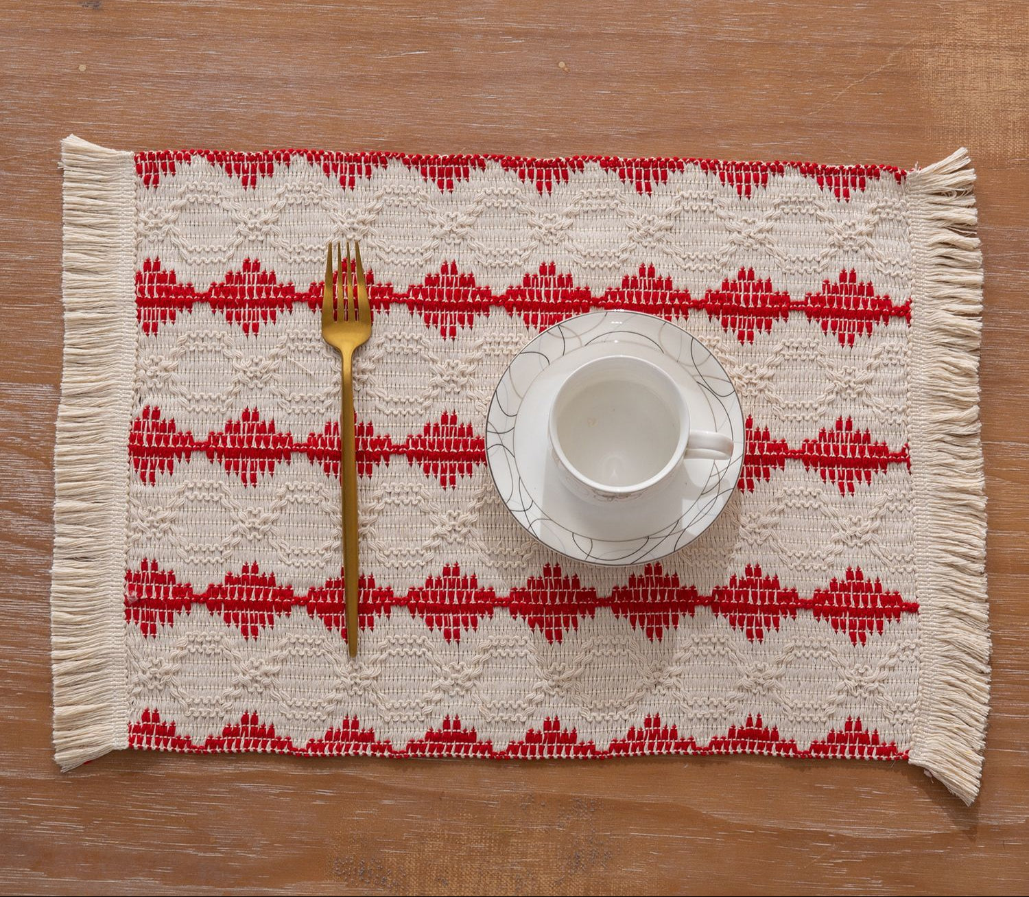 Placemat with red geometric pattern on a wooden table with a cup and fork.