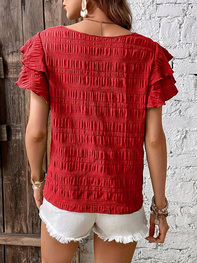 Person wearing a red textured top and white shorts against a rustic wooden and white brick wall.