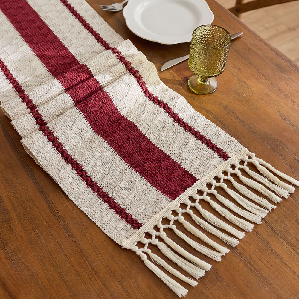 Red and white striped table runner with fringes on a wooden table.