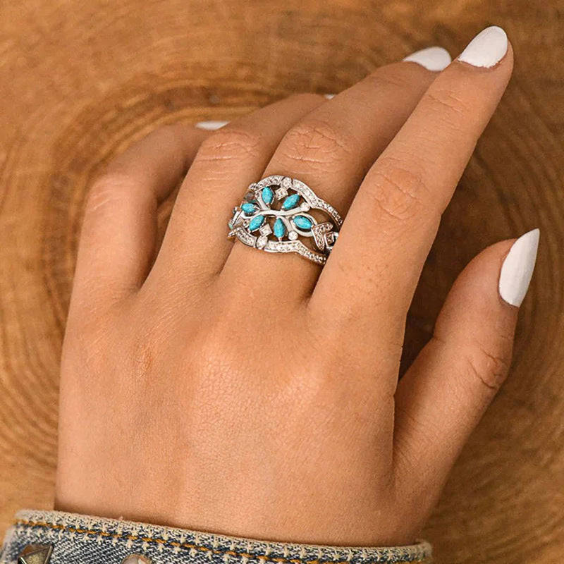Hand wearing a silver ring with turquoise stones on a wooden surface