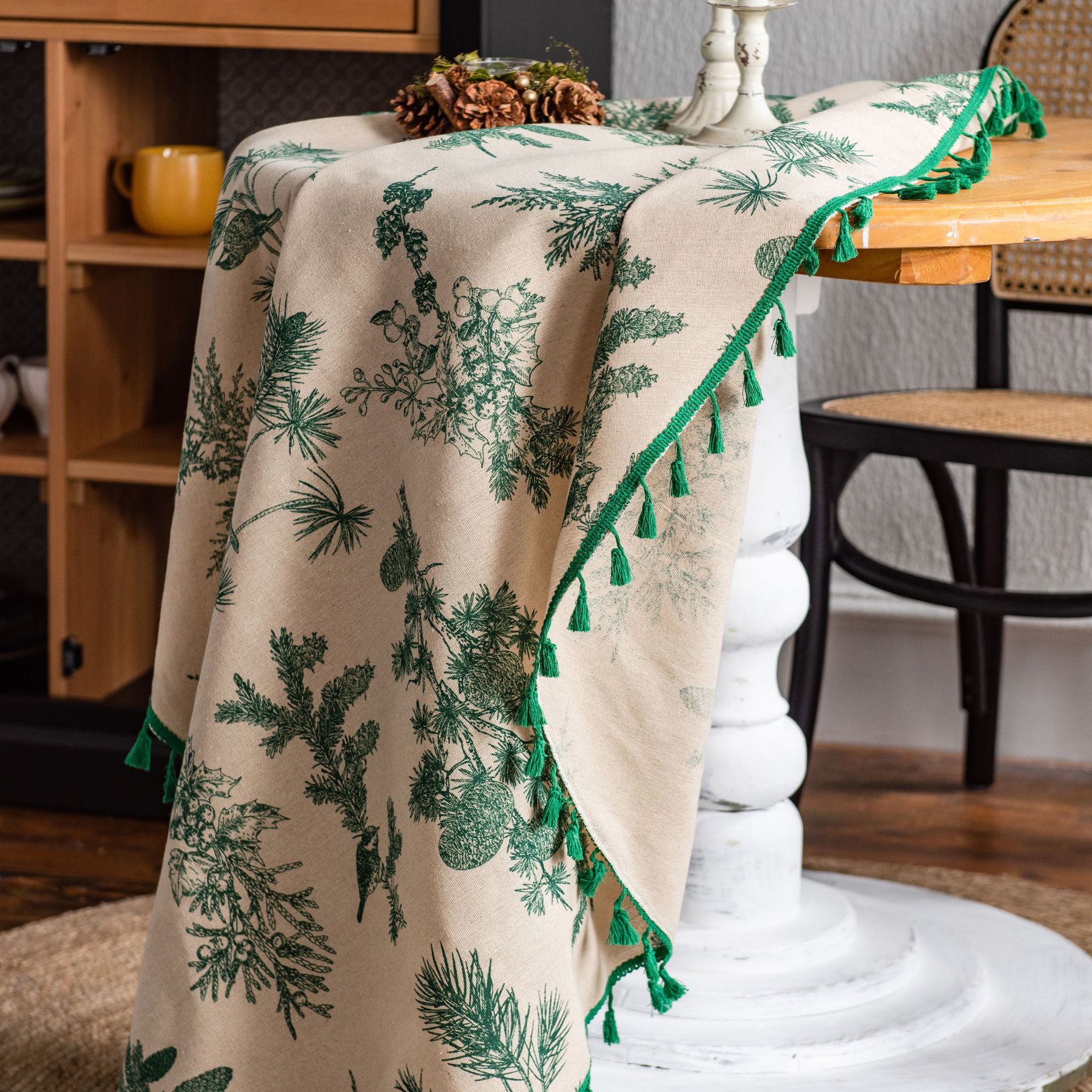 Beige tablecloth with green leaf pattern and tassels draped over a table.