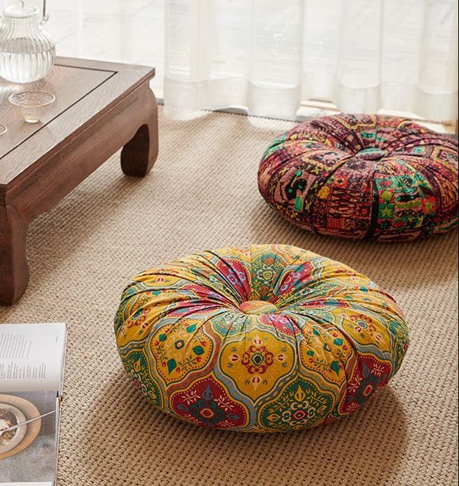 Decorative round cushions on a beige rug with a wooden table and white curtains in the background.