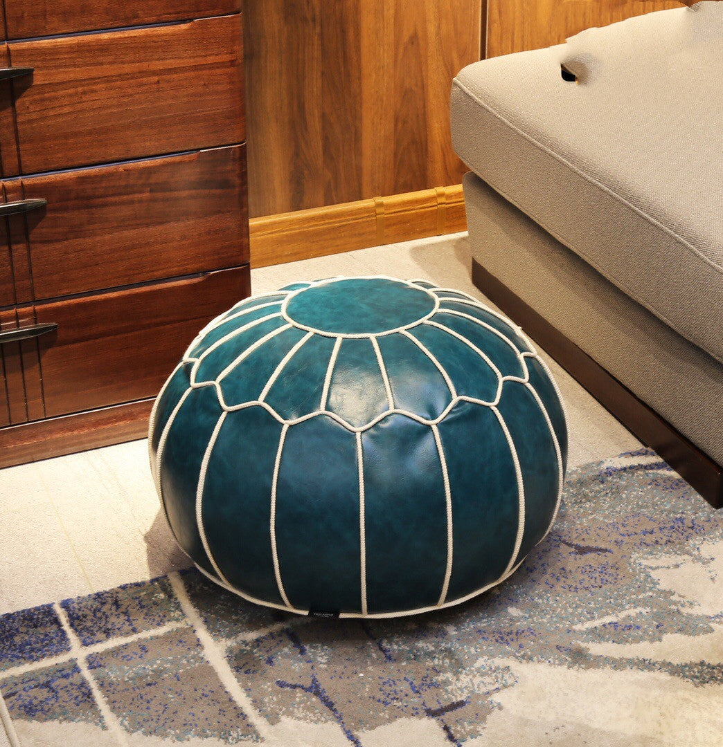 Blue leather pouf on a patterned rug next to a wooden cabinet and beige ottoman.