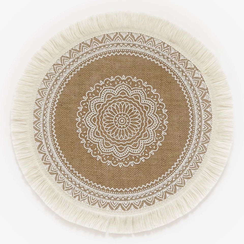 Round beige rug with white mandala design and fringes on a white background