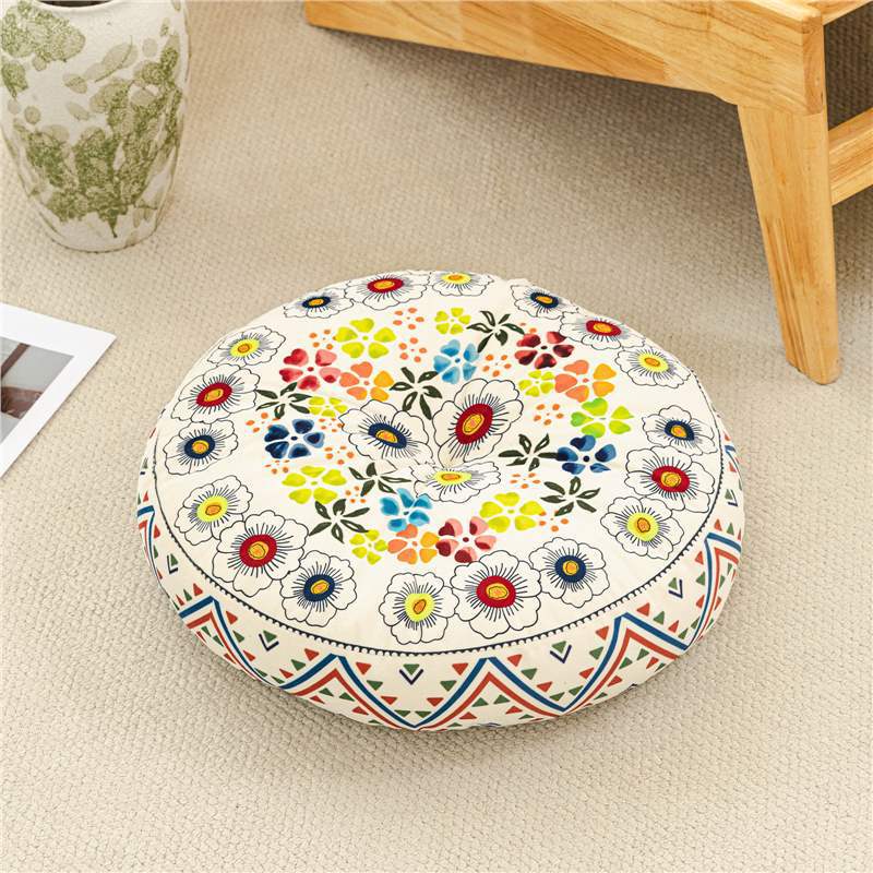Round floral patterned cushion on a beige floor with a wooden table and vase in the background.
