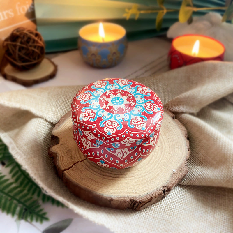 Decorative red and blue patterned box candle on a wooden surface with candles in the background