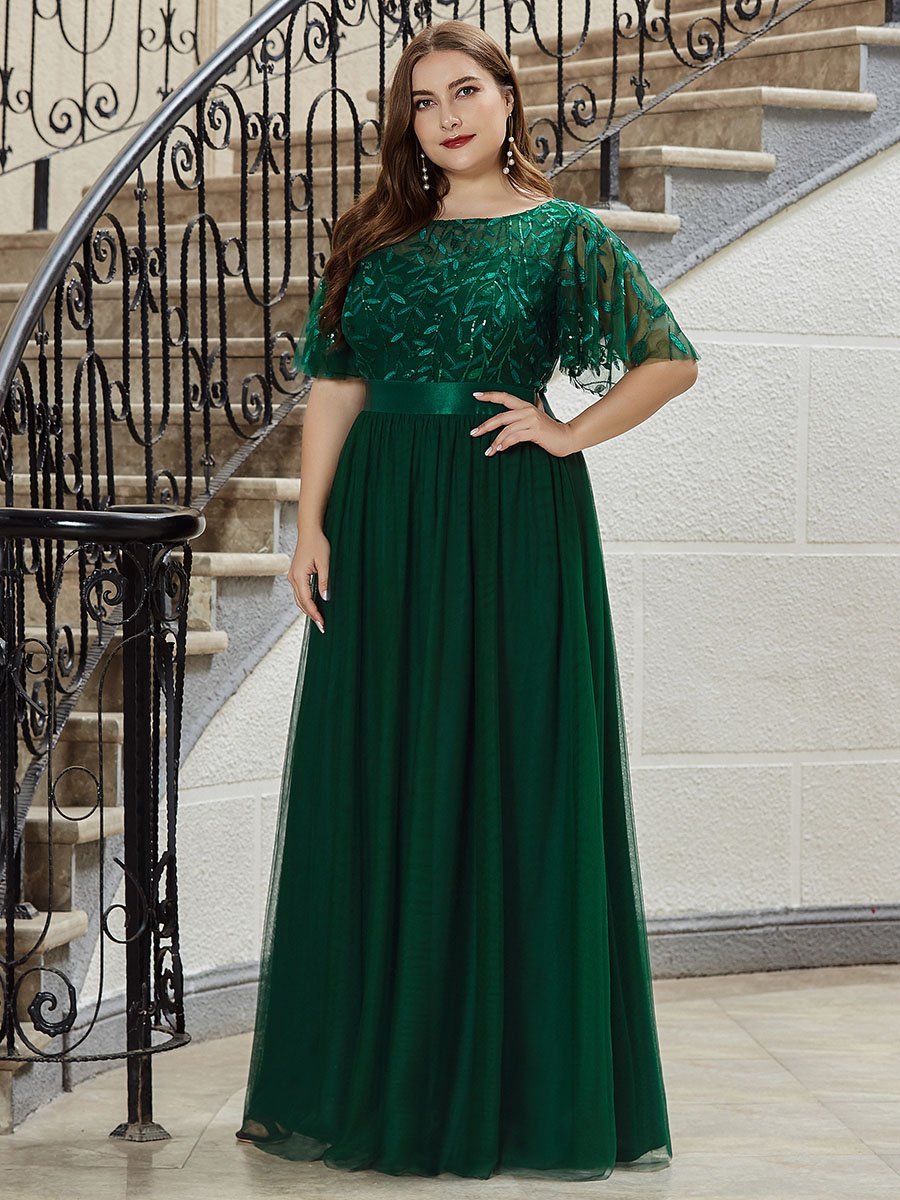 Woman in a green evening gown standing on a staircase.