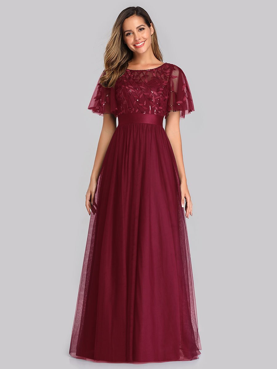 Woman wearing a burgundy evening gown with lace top on a gray background