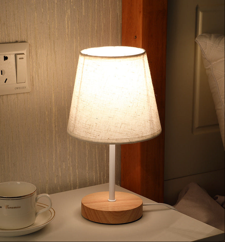 Table lamp with wooden base on a nightstand next to a cup and saucer.