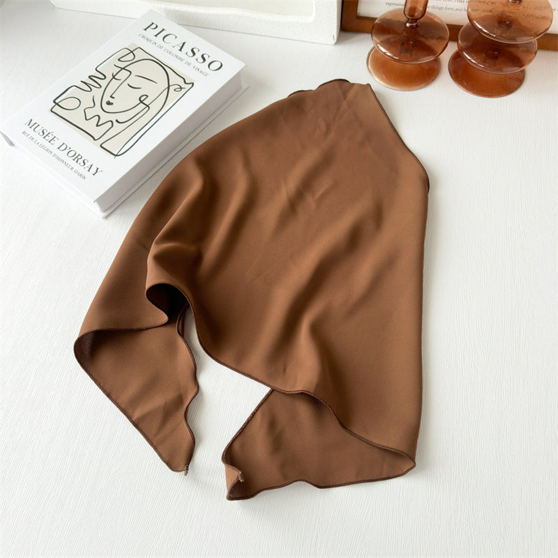 Brown silk scarf on a white surface with a book and decorative items in the background