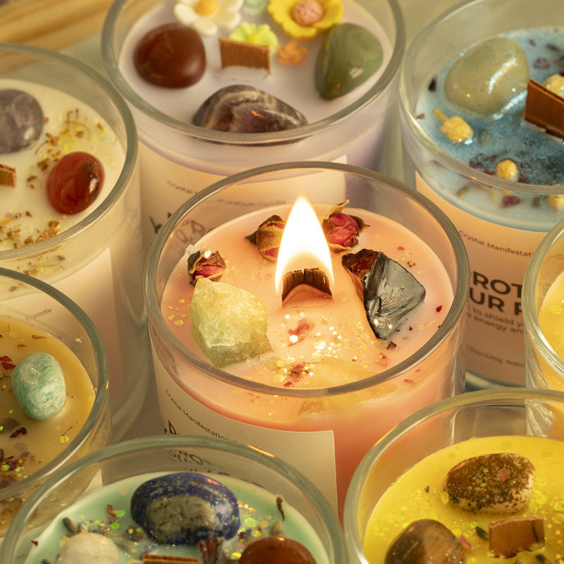Decorative candles with embedded stones and flowers, some lit, on a wooden surface.