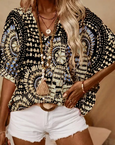 Person wearing a black and gold patterned top with white shorts, standing against a neutral background.