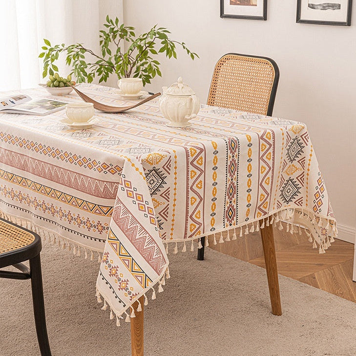 Table with a patterned tablecloth in a room with chairs and decor.