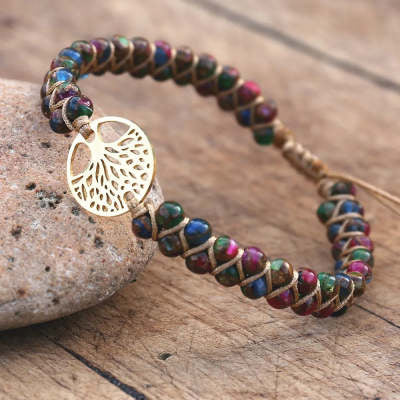 Multicolored beaded bracelet with a gold tree of life charm on a wooden surface