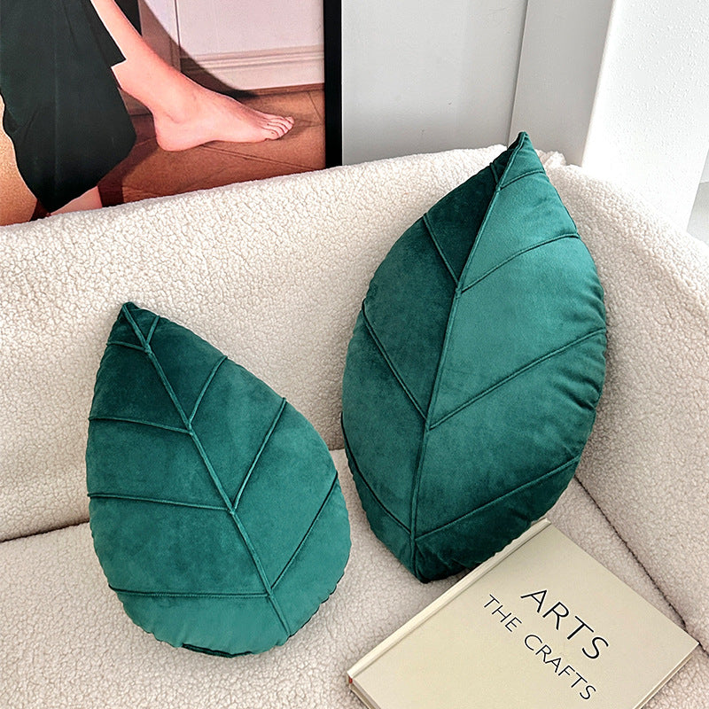 Two green leaf-shaped cushions on a beige sofa with a book titled 'The Arts' in the background.
