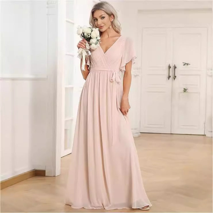 Woman in a long pink dress holding flowers indoors.