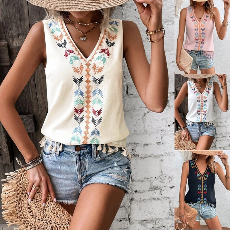 Woman wearing a sleeveless embroidered top and denim shorts with a straw hat and bag.